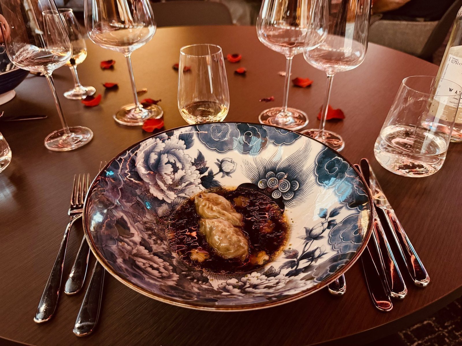 Ein traditionelles Gericht wird präsentiert: zwei gefüllte Teigtaschen in einer dunklen Soße auf einem eleganten, blau weißen Porzellanteller