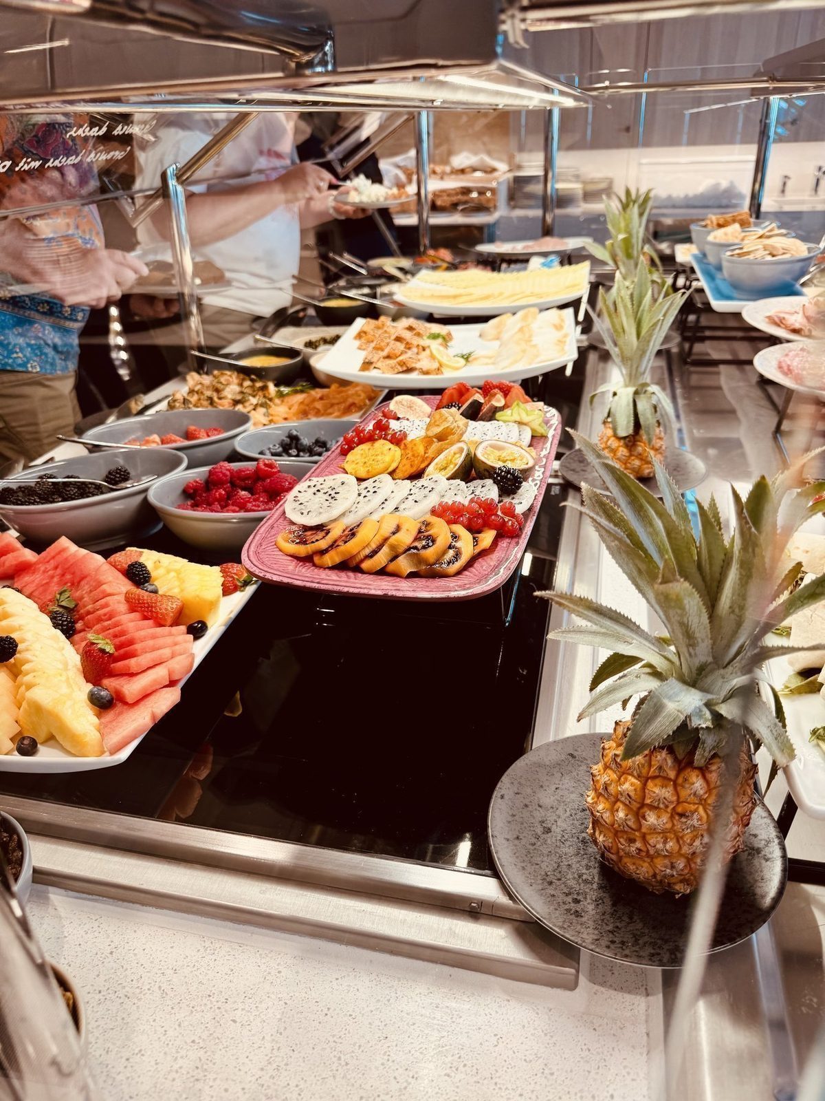 Ein Buffetbord mit frischem Obst wie Wassermelone, Ananas, Bananen und Beeren ist sichtbar