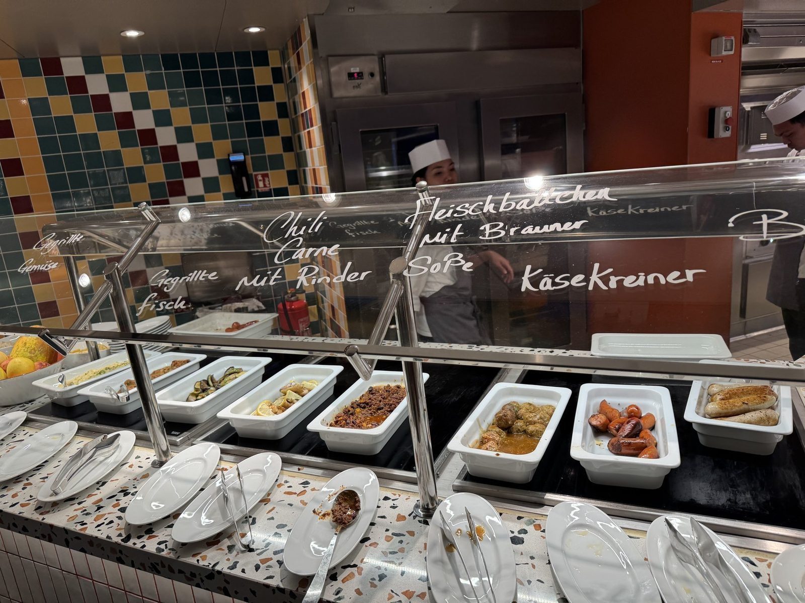 Verschiedene Gerichte sind in weißen Schalen präsentiert, darunter Fleischbällchen, Chili Carne und Käsekreiner