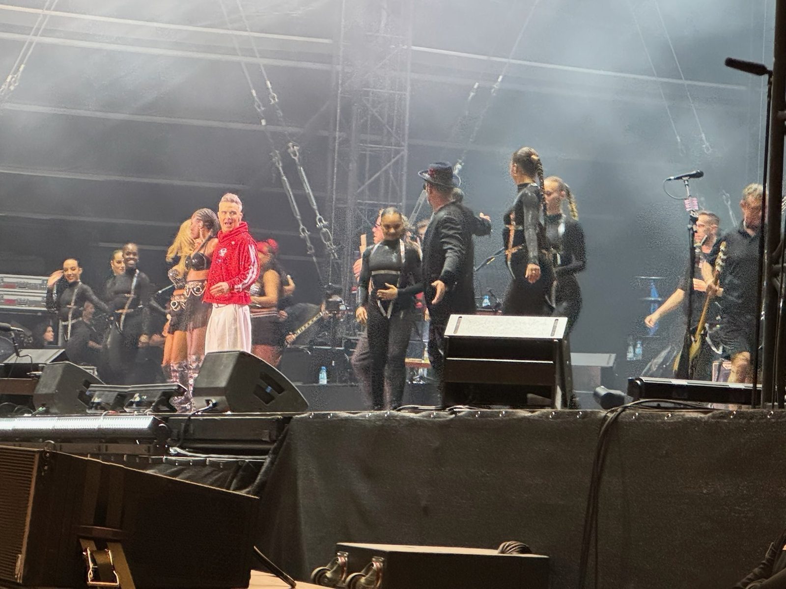 Ein Musiker in einem roten Oberteil steht im Vordergrund eines Konzerts mit anderen Musikern und Tänzerinnen im Hintergrund