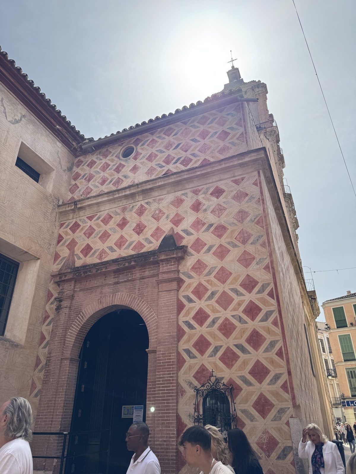 Ein Gebäude mit einer auffälligen Fassade aus einem farbigen Mosaikmuster ist im Vordergrund zu sehen, während Menschen in der Nähe stehen