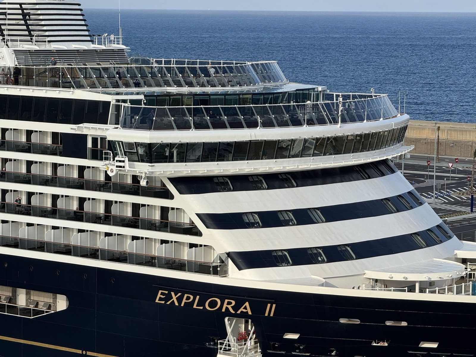 Ein großes Kreuzfahrtschiff mit dem Namen "Explora II" ist im Vordergrund zu sehen, während es an einem Hafen liegt