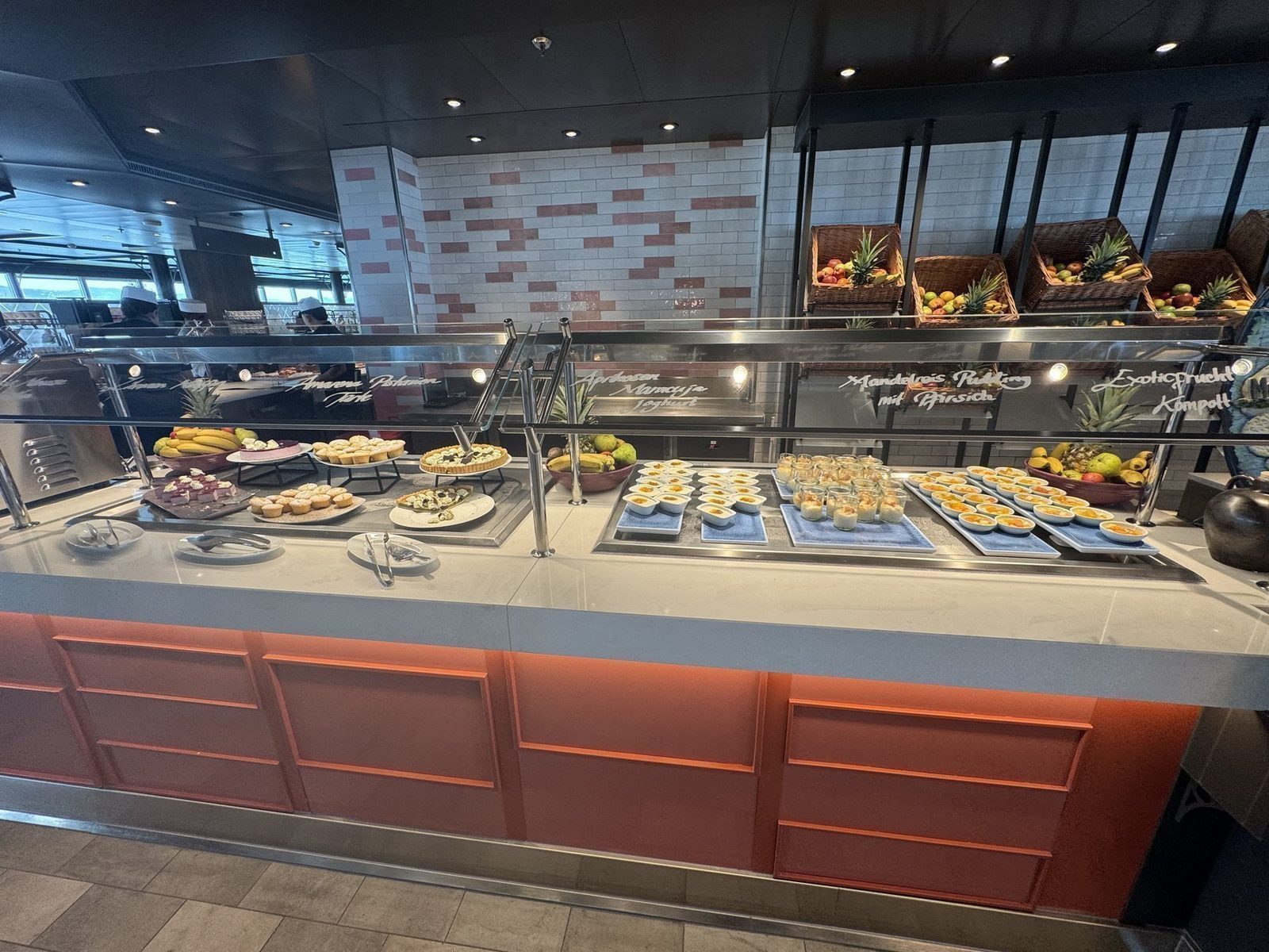 Ein Frühstücksbuffet bietet eine Vielzahl von Desserts in Gläsern sowie frisches Obst wie Bananen, Ananas und Äpfel