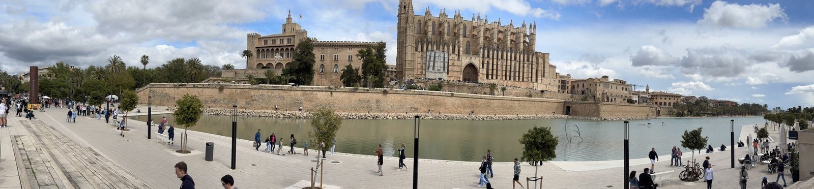 Ein Panorama zeigt die Kathedrale von Palma mit ihrem markanten Turm und gotischen Dach vor einer Mauer aus Stein