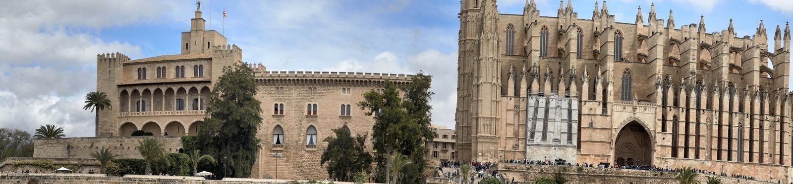 Eine gotische Kathedrale mit markanten Türmen und einem angrenzenden Palast mit Arkaden und Zinnen