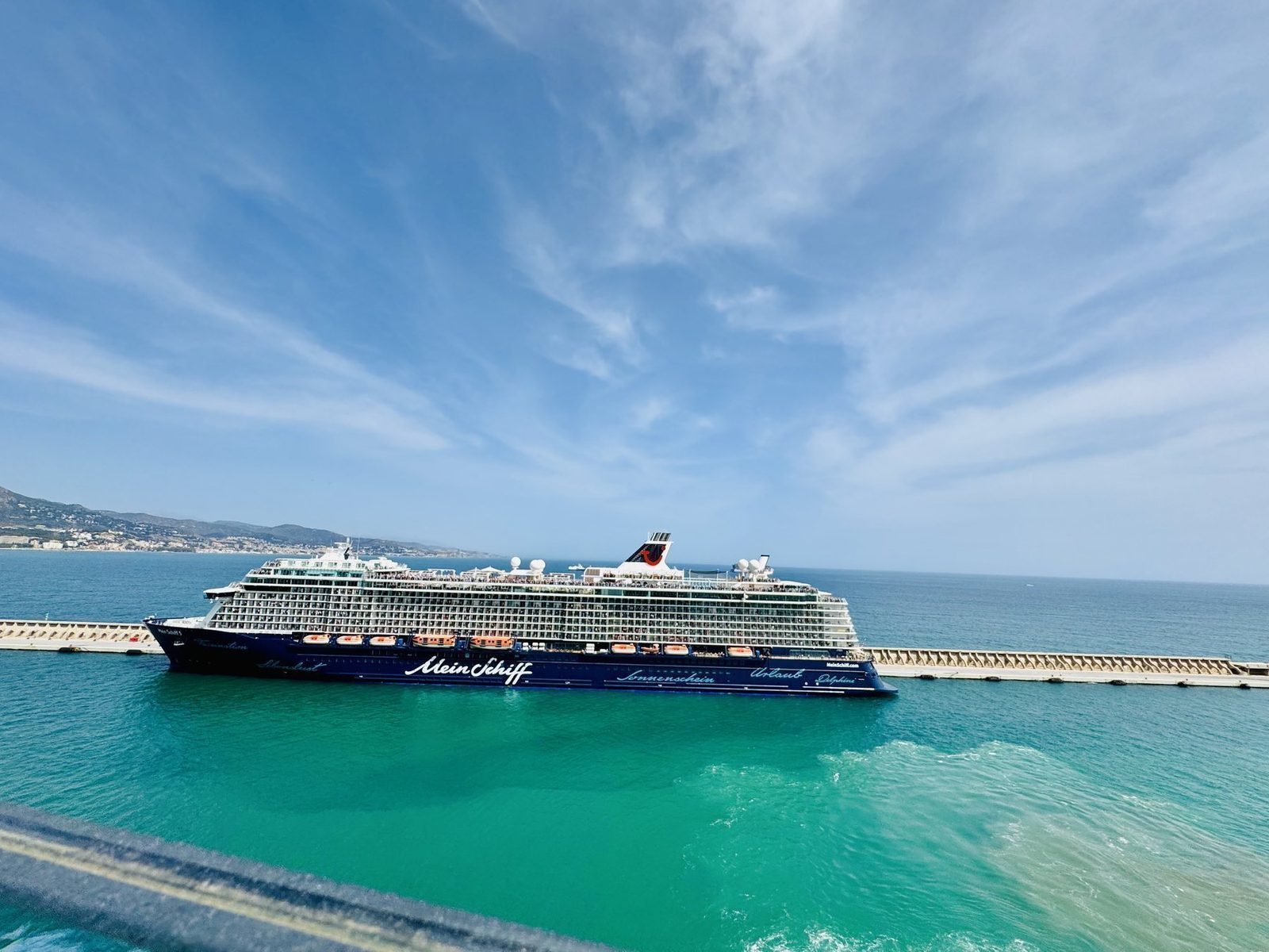 Ein großes Kreuzfahrtschiff liegt ruhig am Kai eines Hafens mit türkisfarbenem Wasser