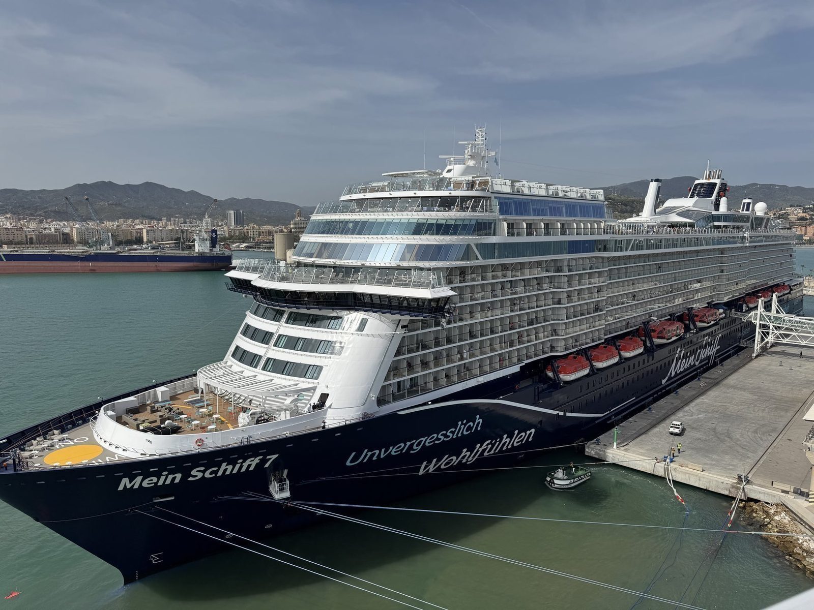 Ein großes Kreuzfahrtschiff mit der Beschriftung "Mein Schiff 7" und dem Slogan "Unvergesslich Wohlfühlen" ist am Kai festgemacht