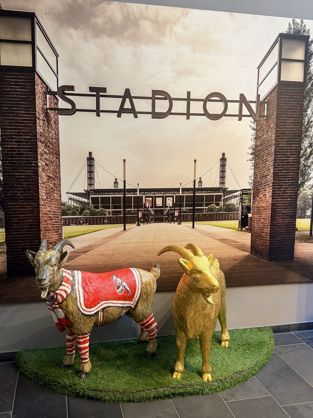 Aus dem Parkhaus grüßten zwei Hennes Figuren vor einer Stadionkulisse: eine im roten Trikot mit Schal, die andere vergoldet