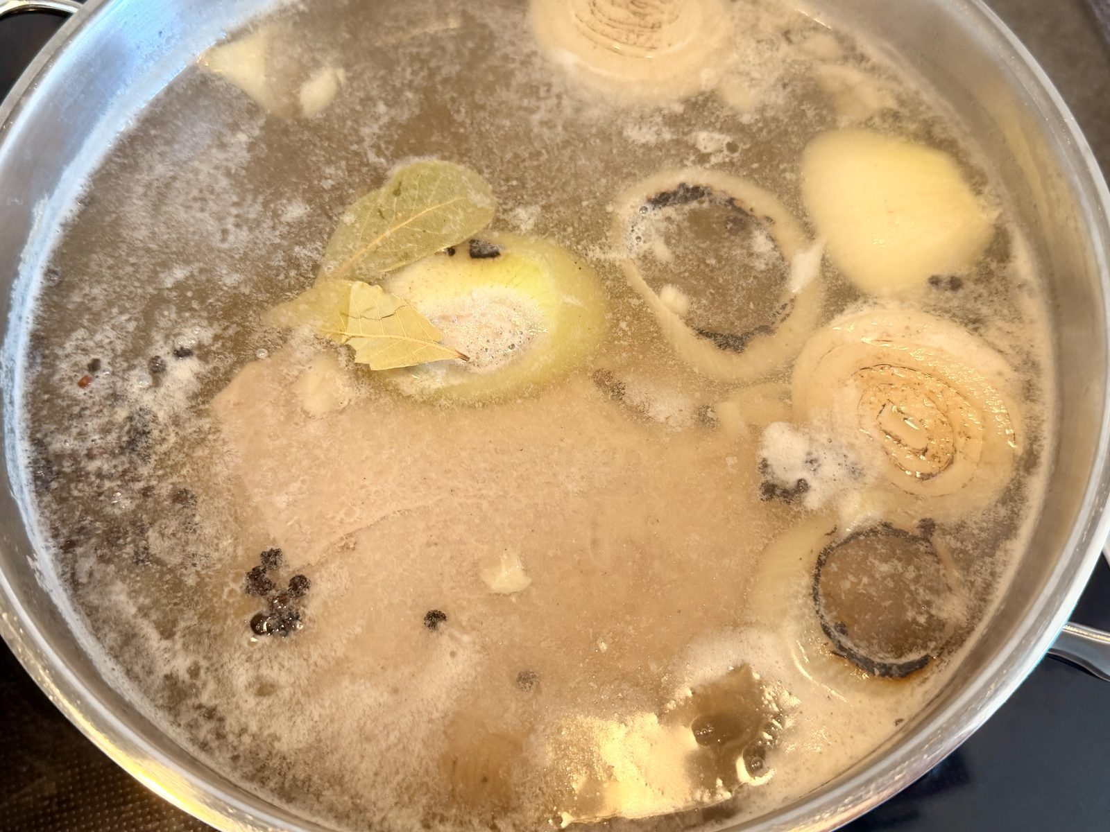 Eine Brühe kocht in einer Pfanne, in der Zwiebelringe, Lorbeerblätter
