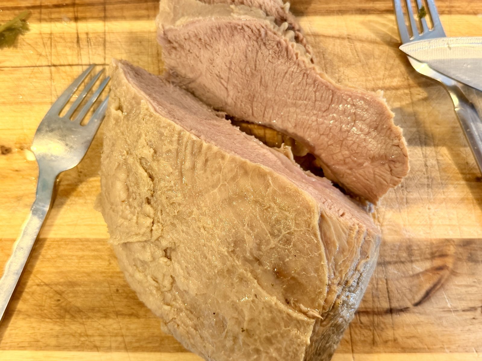 Auf einem Holzbrett liegt ein geschnittenes, gekochtes Fleischstück mit deutlich