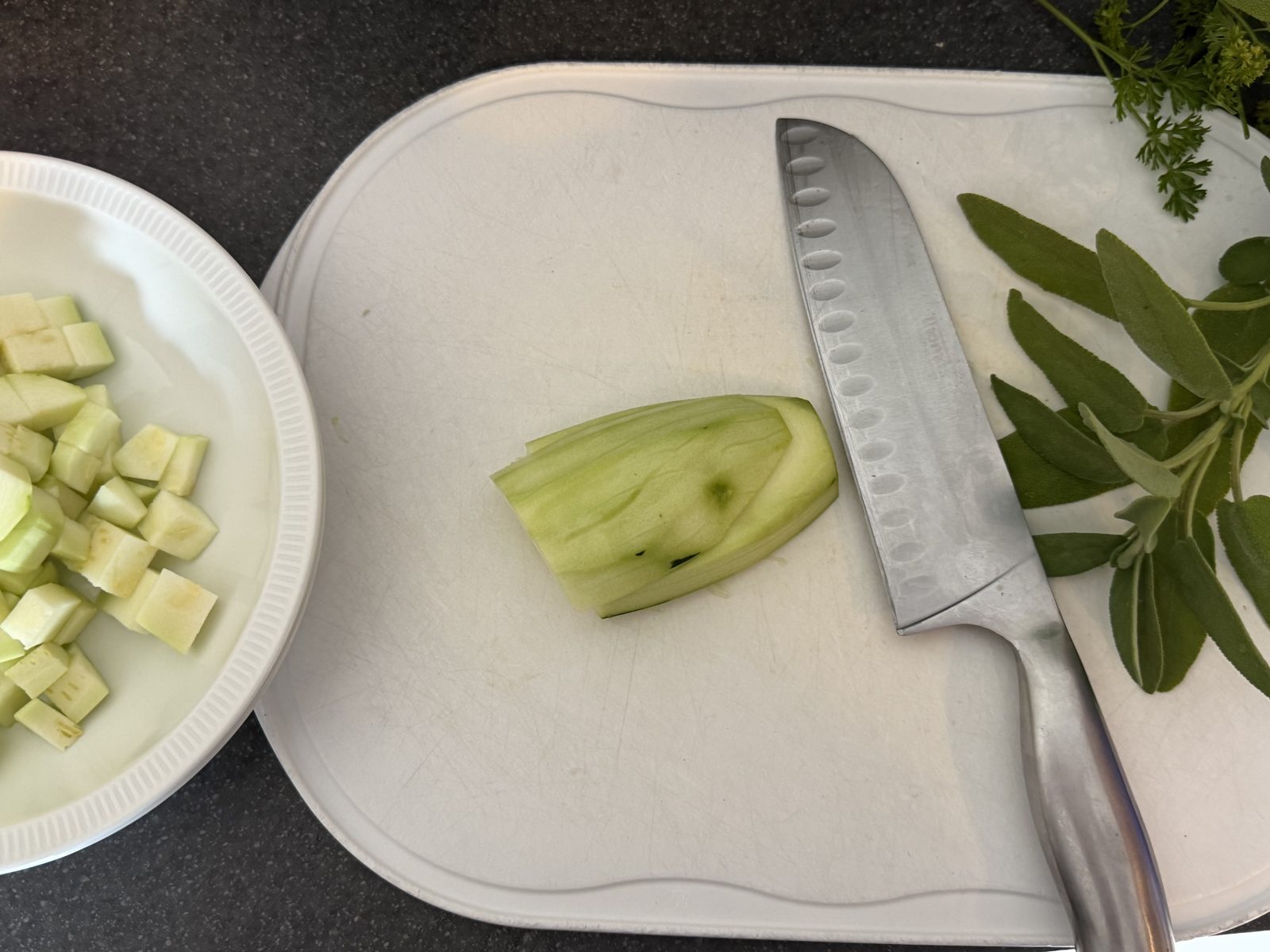 Eine Gurke liegt auf einer weißen Schneideplatte neben einem Messer