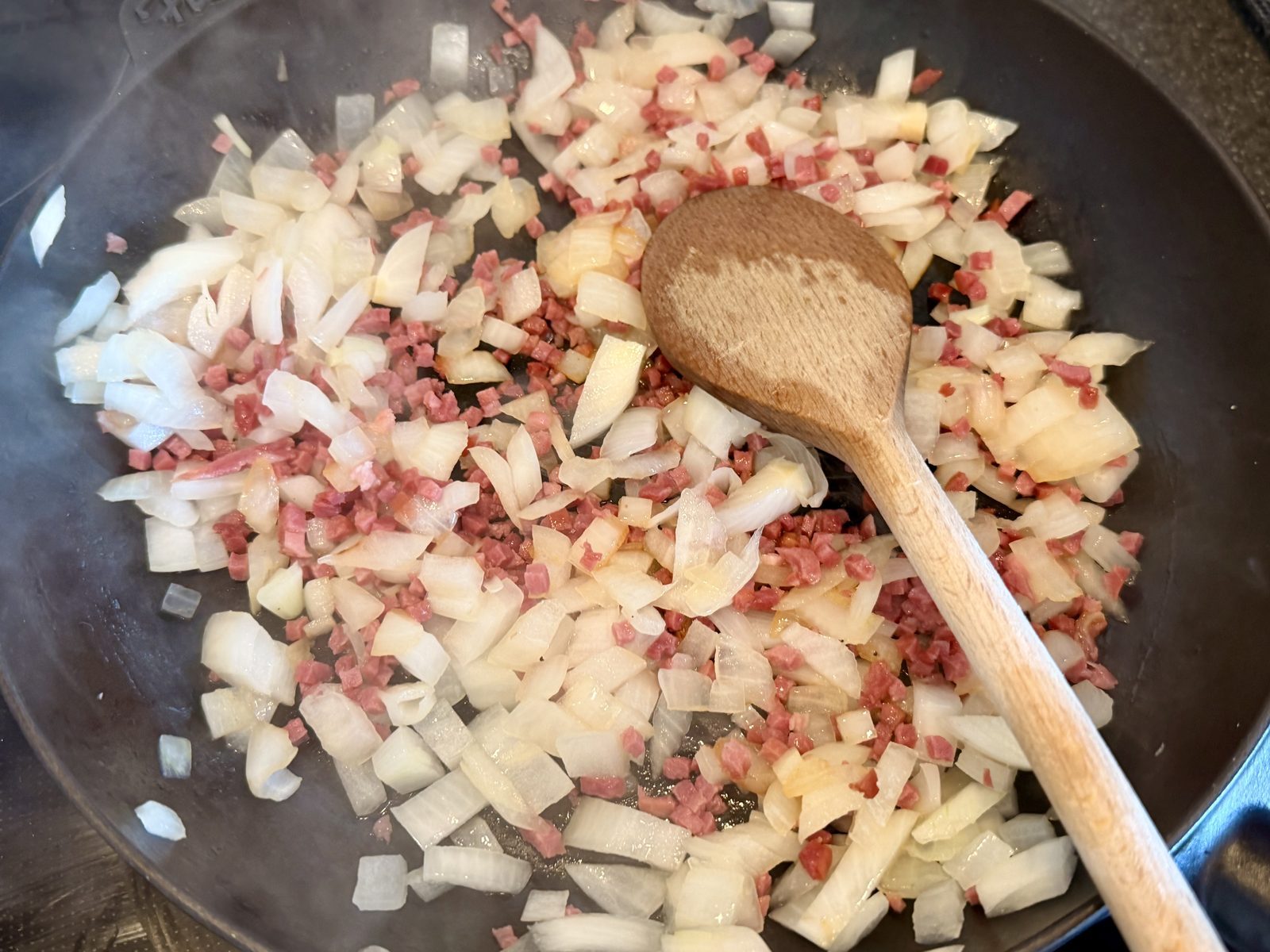 In einer schwarzen Pfanne werden kleine Würfel von Zwiebeln und rote Würfel von Wurst